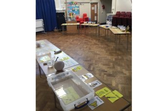 A school hall with tables of activity equipment and Makaton symbols